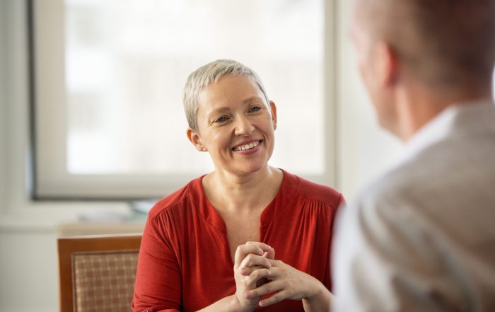 A woman with her hands clasped smiling at a man.