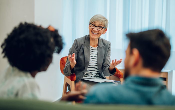 Attentive mature female doctor is listening to her clients mental and marriage problems and taking notes in her office while taking notes. Psychotherapy consultation. Copy space.
