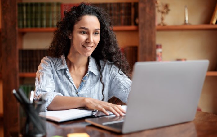 Doing Project. Portrait of curly young woman using laptop computer and typing on keyboard, writer sitting at table. Female manager working remotely or studying online at home, telecommuting